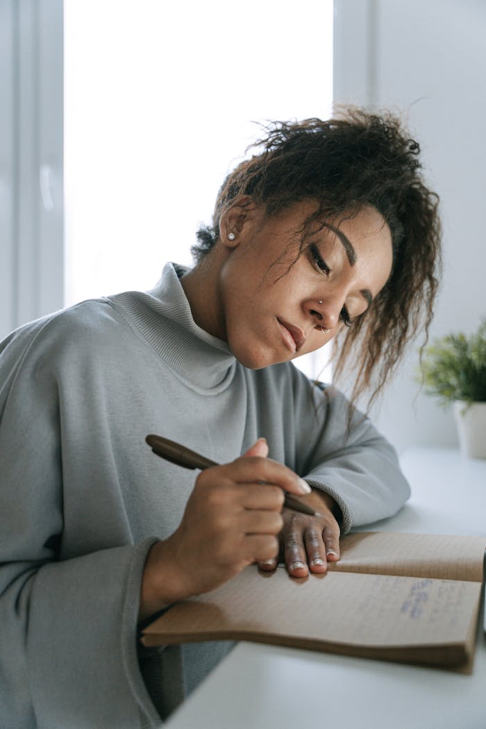 African American woman with afro hair writing in a notebook indoors.
