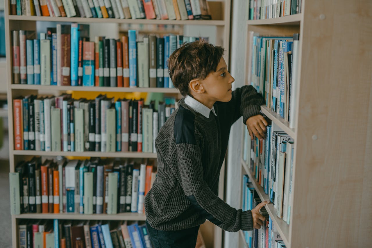Boy in a sweater browsing books in a cozy library, focused study.